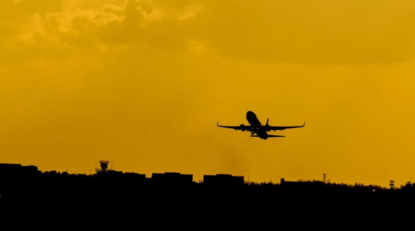 Silhouette of an aircraft climbing into a golden-hour sky
