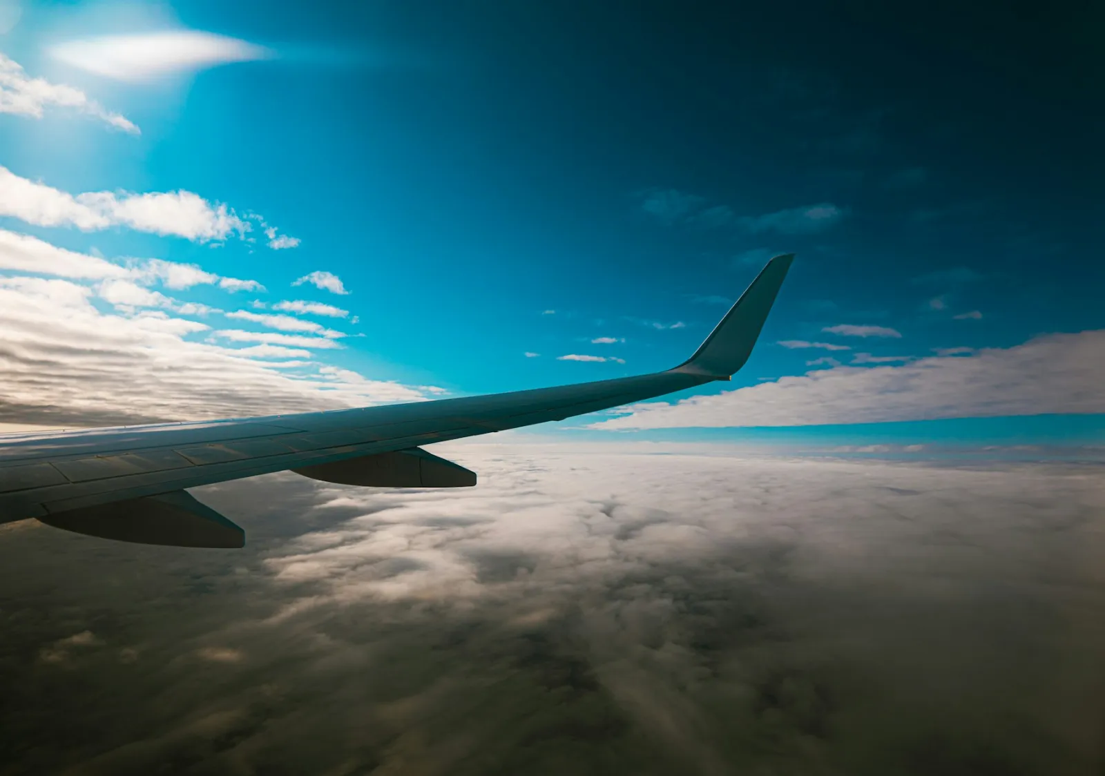 Airplane wing above clouds under a clear blue sky